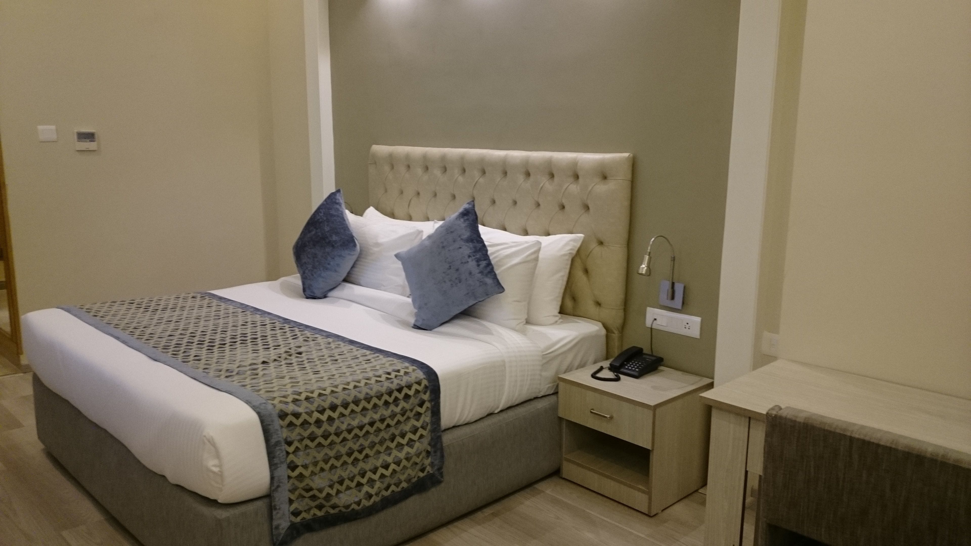 A neatly made bed with a patterned throw, a bedside table with a lamp, and a phone.