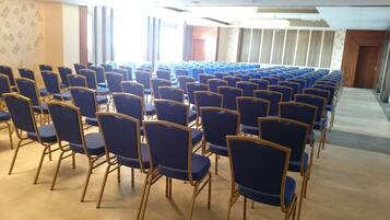 Sinisiä tuoleja on asetettu riveihin konferenssihuoneeseen, jossa on matto lattialla ja kuvioitu seinä.