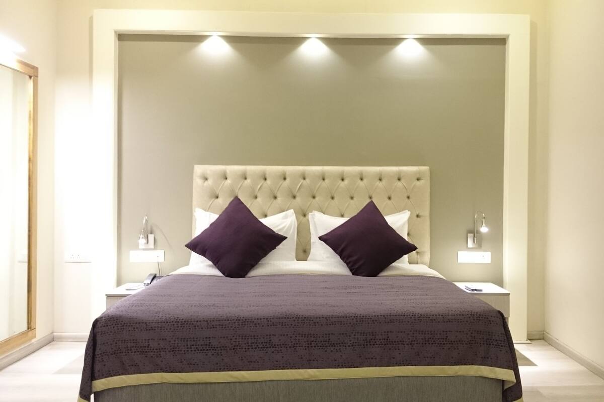 Quarto com cabeceira estofada, duas mesas de cabeceira com luminárias e uma cama grande com colcha estampada e duas almofadas.