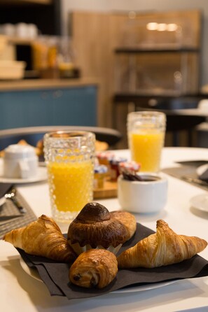A breakfast setting with croissants and orange juice on a table. - The Originals Boutique, Hôtel des Sources (Pougues-les-Eaux)