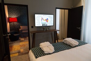 Une chambre d’hôtel avec un lit, deux serviettes, un téléviseur fixé au mur, une lampe rouge, une chaise et un tapis à motifs.