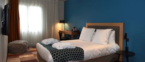A hotel room with a bed, a nightstand, a lamp, a TV, and a window with curtains.