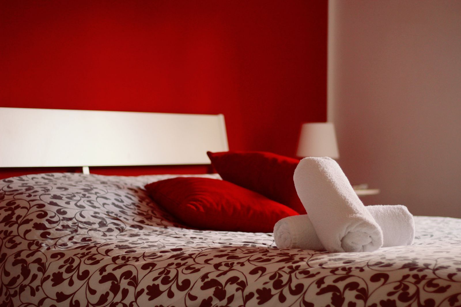 Un lit bien fait, recouvert d ’une couvre-lit à motifs, avec deux oreillers rouges et une serviette blanche roulée.