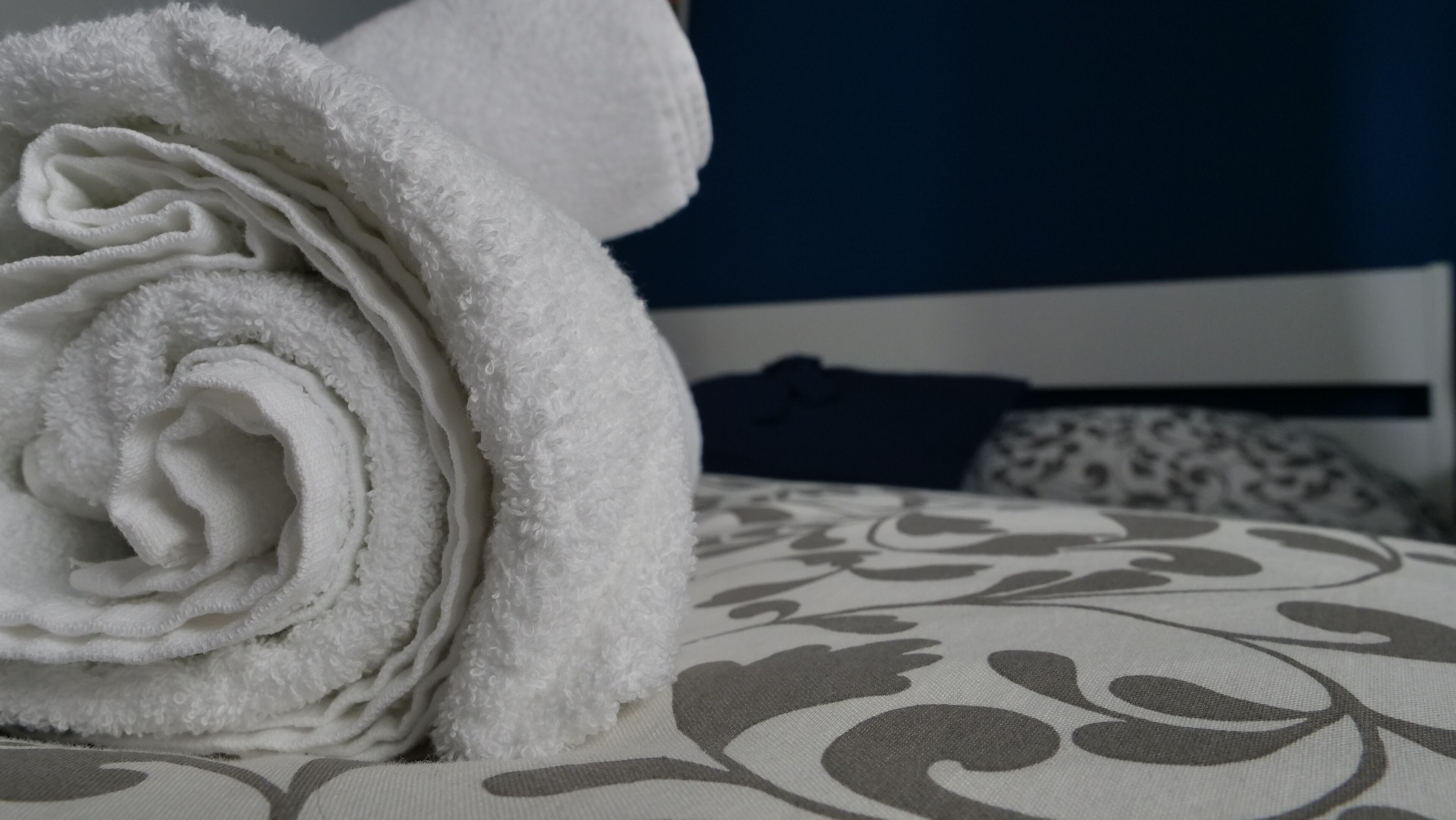 A neatly rolled white towel on a bed with a patterned bedspread.