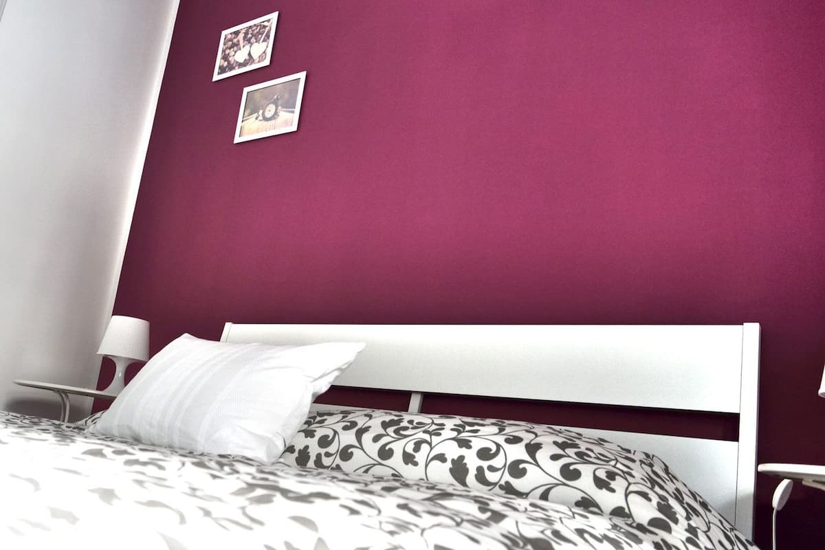 A bedroom with a white bed, patterned bedding, a white headboard, and a red wall.