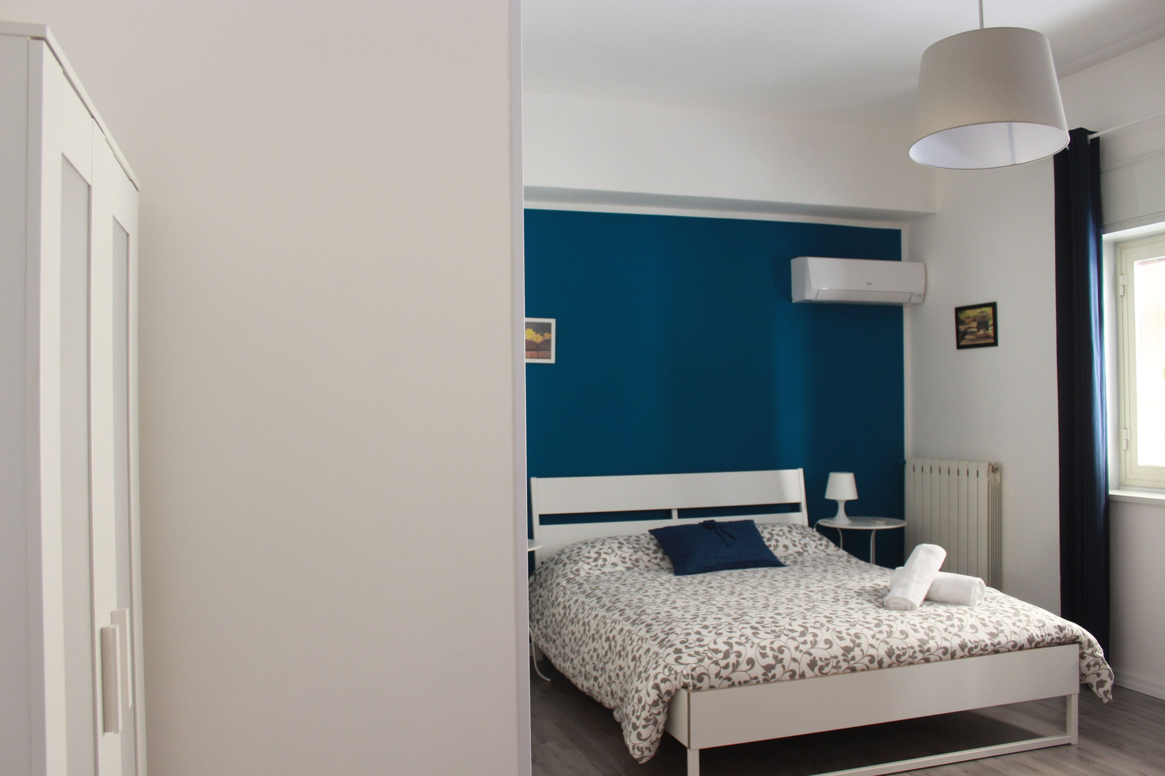 A bedroom with a bed, a bedside table, a lamp, and a window with curtains.