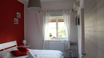 A bedroom with a bed, a window with curtains, a chair, and a radiator.
