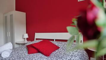 A bed with a patterned bedspread, a red pillow, and a white headboard.