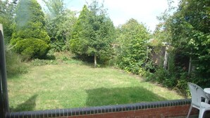 A patio area with a brick wall and a grassy yard. - Draycott Guest House (Harrow)