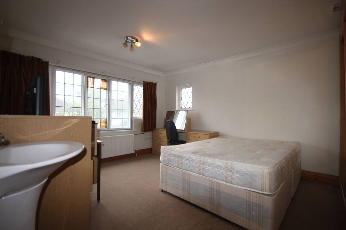 A bedroom with a bed, a desk, a chair, a window, and a radiator.