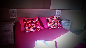 A bed with two colorful floral pillows, a wooden nightstand, and a dresser.
