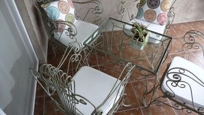 A small, enclosed patio area with a glass table surrounded by metal chairs with white cushions.