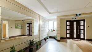 Un couloir propre et bien éclairé, agrémenté de plantes en pot, d’un miroir et d’un panneau de signalisation indiquant clairement la sortie.