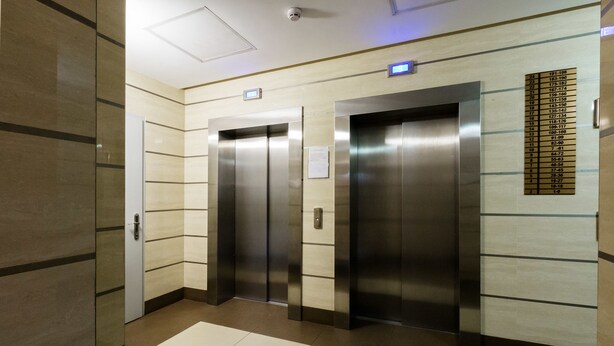 Un espace comprenant deux ascenseurs, un écran numérique et un indicateur d’étage.