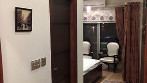 A hotel room with a bed, a chair, a window with curtains, a door, and a small rug. - luxes Inn (Rawalpindi)