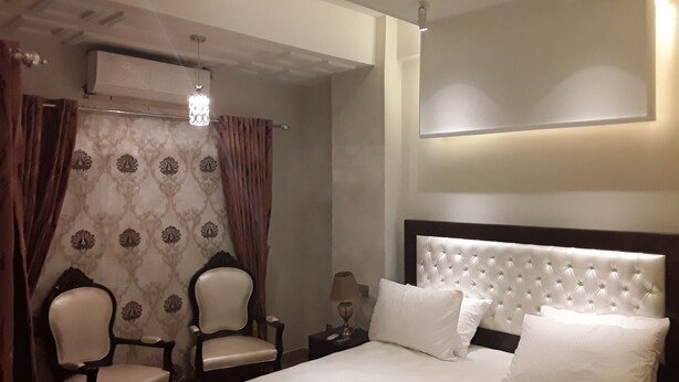 A hotel room with a large bed, two armchairs, a nightstand, and a wall-mounted air conditioning unit. - luxes Inn (Rawalpindi)