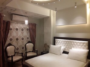 Habitación de hotel con una cama grande, dos sillones, una mesita de noche y un aire acondicionado de pared.