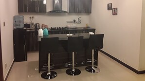 A modern kitchen with a central island, black bar stools, and pendant lighting. - luxes Inn (Rawalpindi)