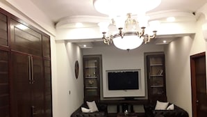 A living room with a dark-colored sofa, a flat-screen TV, and a chandelier. - luxes Inn (Rawalpindi)