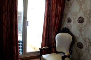 Una habitación con una silla cerca de una ventana, cortinas y papel tapiz estampado.