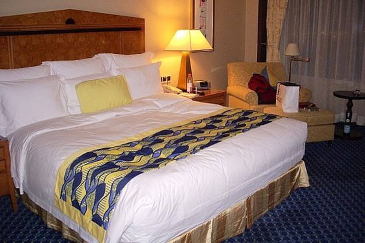 A hotel room with a large bed, a bedside table with a lamp, a chair, and a small table.
