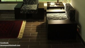 Una sala de estar acogedora con un ventanal grande, un sofá estampado, una mesita con una lámpara y una alfombra roja.