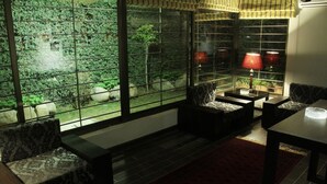 Una habitación con un amplio ventanal que da a un jardín, un sofá, una mesa con una lámpara y una alfombra roja.