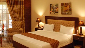 Una habitación de hotel con una cama grande, dos sillones, una mesa de centro de vidrio y dos lámparas de noche.