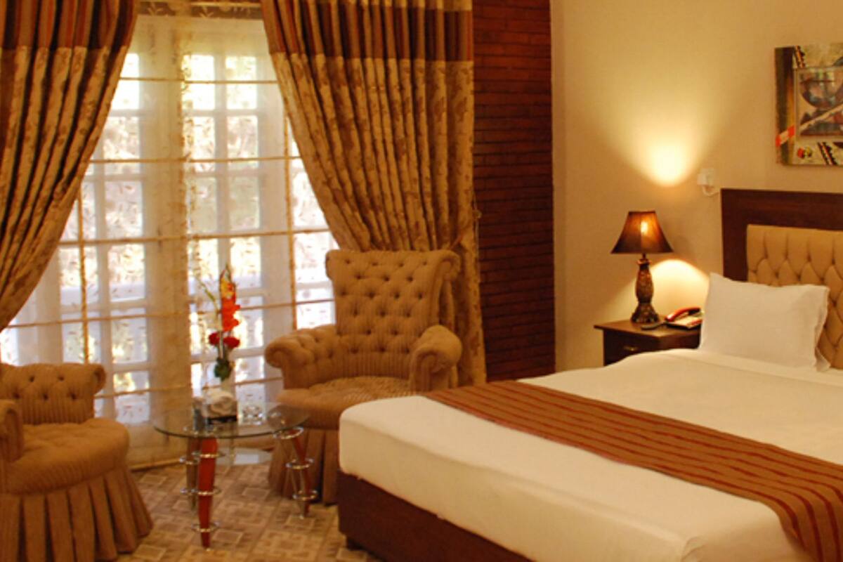 A hotel room with a large bed, two armchairs, a glass coffee table, and two bedside lamps.