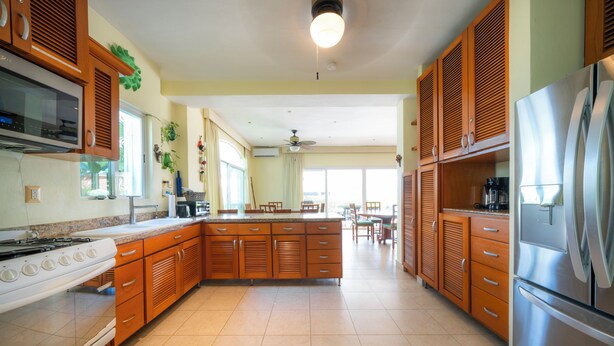 A spacious kitchen with wooden cabinets, a large island, a stainless steel refrigerator, and a gas stove. - Pura Vida by NAS (Playa del Carmen)