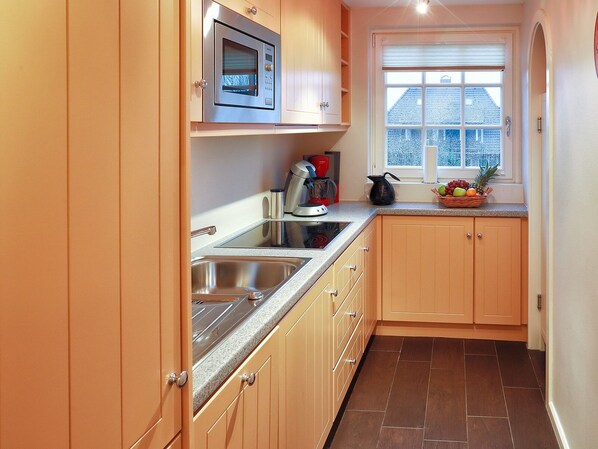A modern kitchen with wooden cabinets, a stainless steel sink, a microwave, and a window with a view of the outside. - Ferienwohnung Biberhüs OG (Sylt)