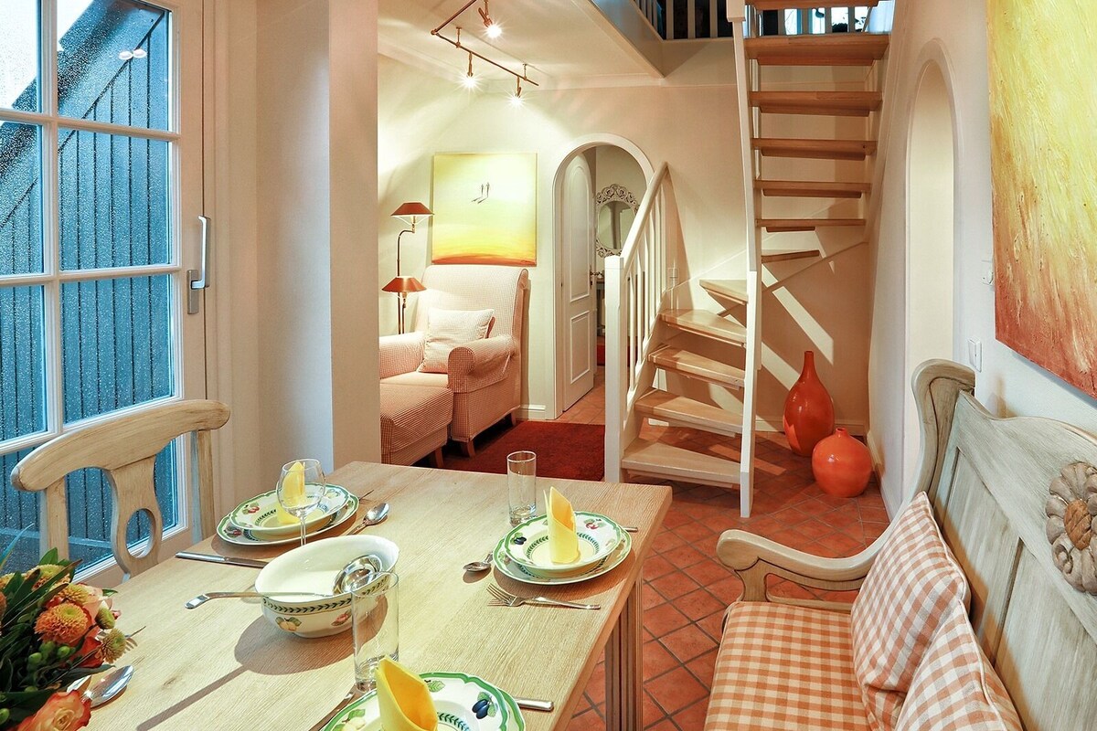 A dining area with a table set for two, a staircase, and a sofa.