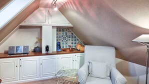 A cozy kitchen with white cabinets, a blue and white tiled backsplash, a coffee machine, and a small table with a plant. - Ferienwohnung Biberhüs OG (Sylt)
