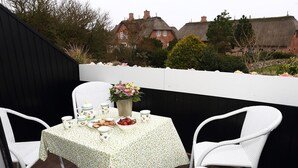 A patio with a table set for tea, surrounded by white wicker chairs. - Ferienwohnung Biberhüs OG (Sylt)