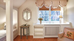 A bedroom with a bed, a bedside table with a lamp, a dresser, a mirror, and a window with curtains. - Ferienwohnung Biberhüs OG (Sylt)