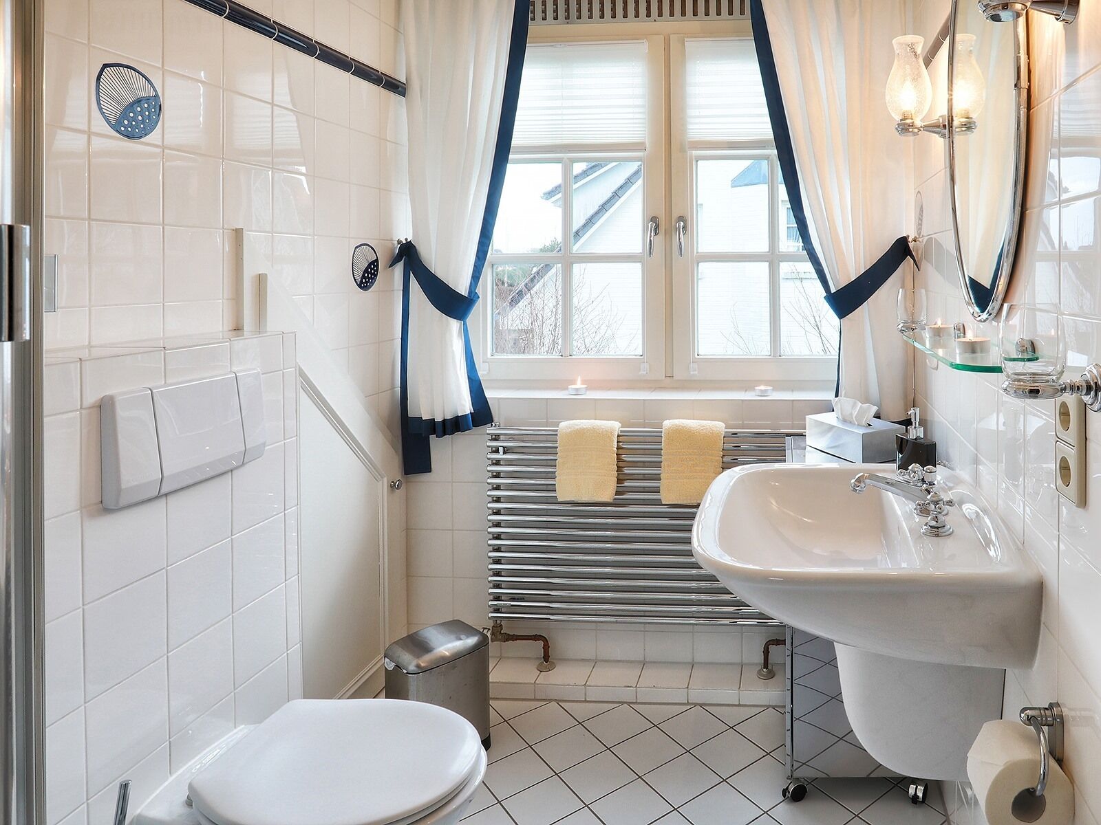 A bathroom with a toilet, bidet, and sink, a window with curtains, and a towel rack.