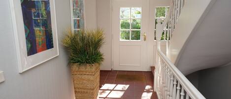 A hallway with a white door, a potted plant, and a staircase with white balusters.