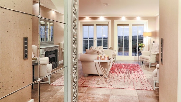 A spacious living room with a fireplace, a large window, and a red carpet. - Ferienwohnung Sönshörn (Sylt)