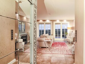 A spacious living room with a fireplace, a large window, and a red carpet. - Ferienwohnung Sönshörn (Sylt)