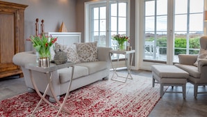 A living room with a white sofa, a coffee table, and a red patterned rug. - Ferienwohnung Sönshörn (Sylt)