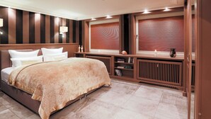 A modern bedroom with a large bed, built-in shelving, and a large window with blinds. - Ferienwohnung Sönshörn (Sylt)
