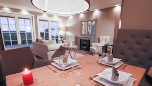 A dining area with a wooden table set for four, a red candle, and a fireplace in the background. - Ferienwohnung Sönshörn (Sylt)