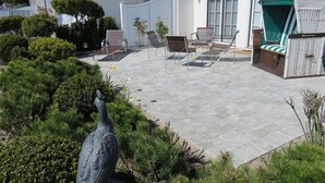 A patio area with stone flooring, outdoor furniture, and a statue. - Ferienwohnung Sönshörn (Sylt)