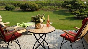 An outdoor patio with a round table, two red cushioned chairs, a vase of flowers, and a bottle of champagne. - Ferienwohnung Sönshörn 8 Rechts (Sylt)