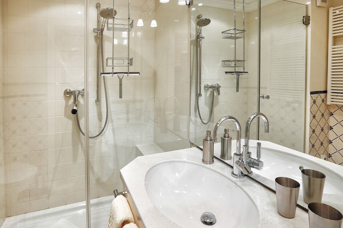 A modern bathroom with a glass-enclosed shower, a large sink with two faucets, and a mirror above the sink.