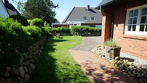 Ein Weg führt zu einem Backsteinhaus mit einer Steinmauer an der Seite und einem Gartenbereich mit einer Bank.