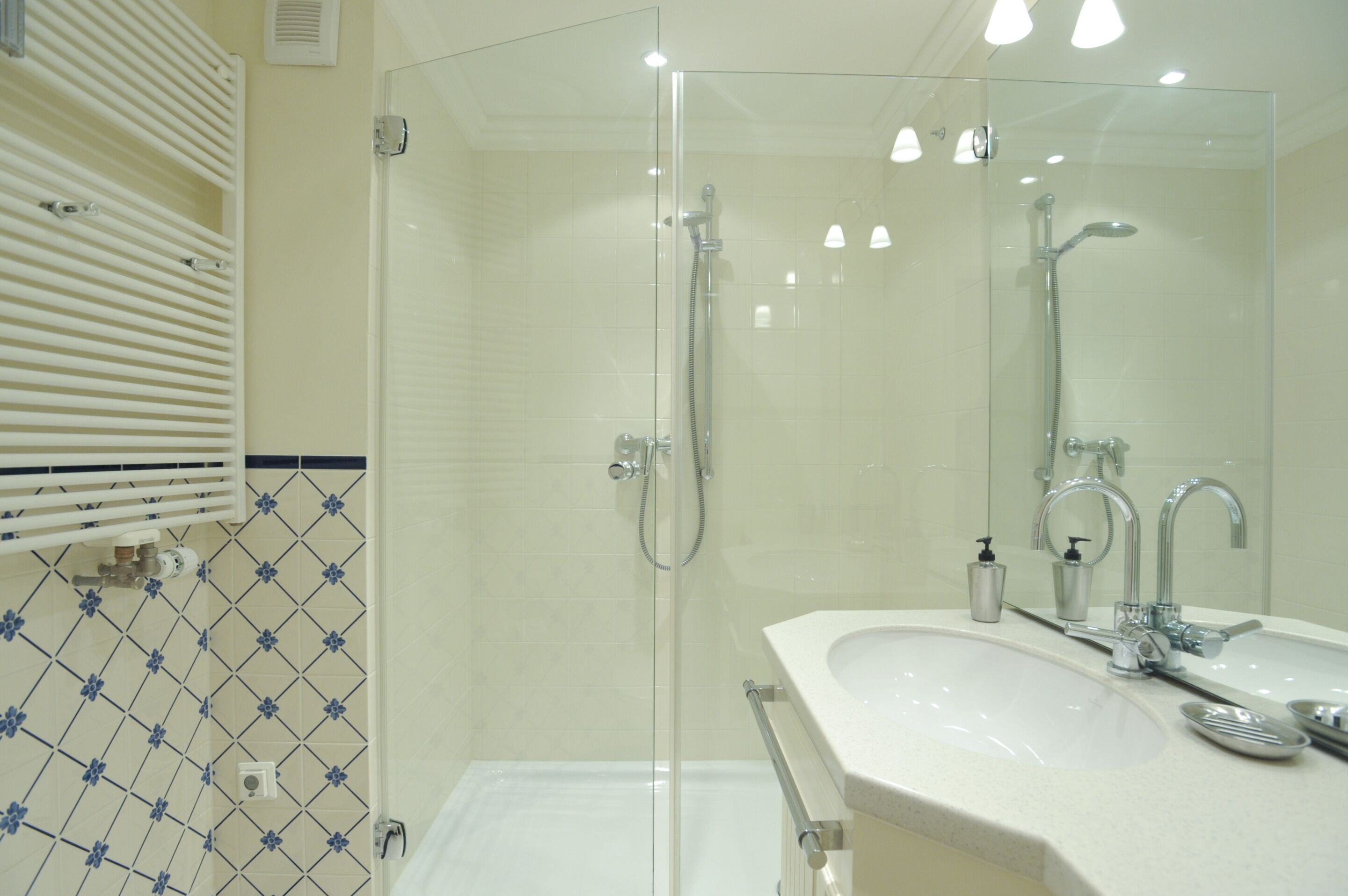 A modern bathroom with a glass-enclosed shower, a white sink with a mirror, and a tiled wall with a blue pattern.