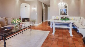 A modern living room with a glass coffee table, a white sofa, and a dining area with a chandelier. - Ferienwohnung Sönshörn 20 (Sylt)