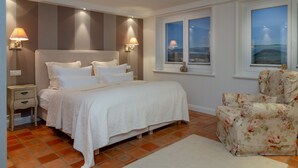 A bedroom with a bed, nightstands, a chair, and two windows with views. - Ferienwohnung Sönshörn 20 (Sylt)