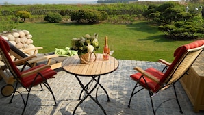 A patio with a round table, two red cushioned chairs, a bottle of champagne, and a vase of flowers. - Ferienwohnung Sönshörn 8 Mitte (Sylt)
